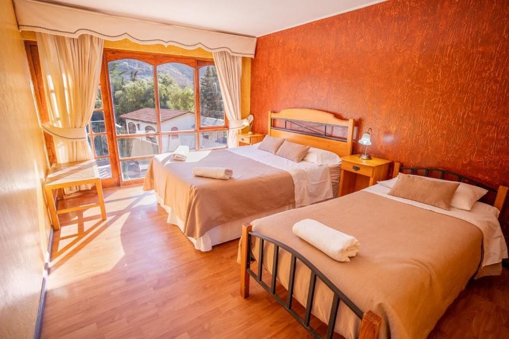 A hotel room with two beds, a wooden desk, and a large window with curtains.