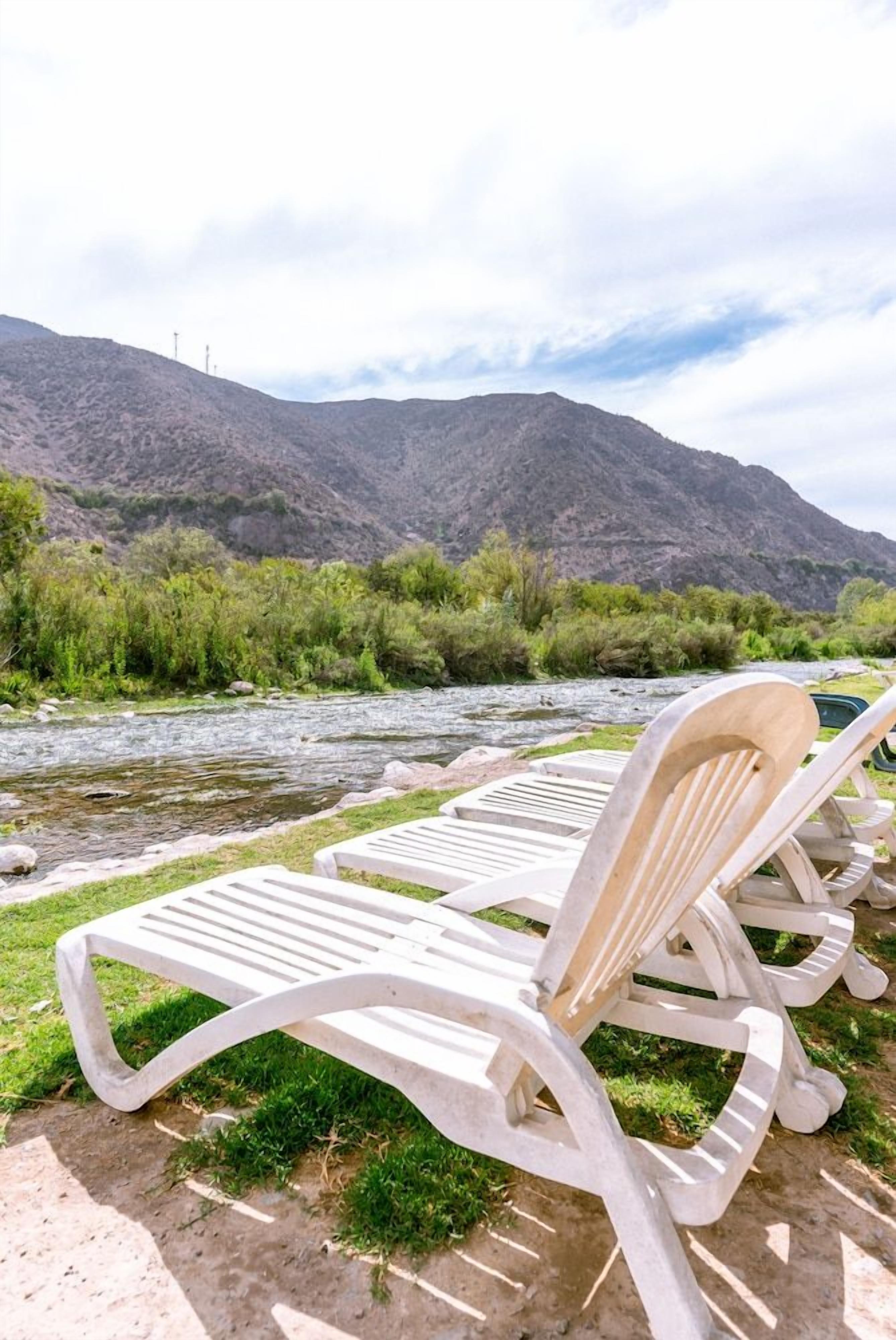 Sillones de exterior junto a un río con montañas al fondo.