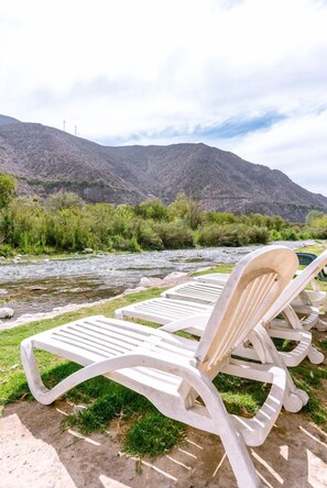 Sillones de exterior junto a un río con montañas al fondo.