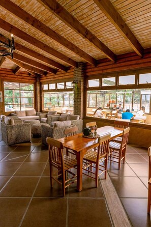 Un intérieur chaleureux avec un plafond en bois, de grandes fenêtres, un coin repas avec une table et des chaises, et un espace détente avec des canapés.