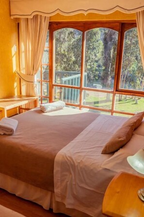 Una habitación con una cama grande, cabecera de madera, mesita de noche y una ventana con cortinas.
