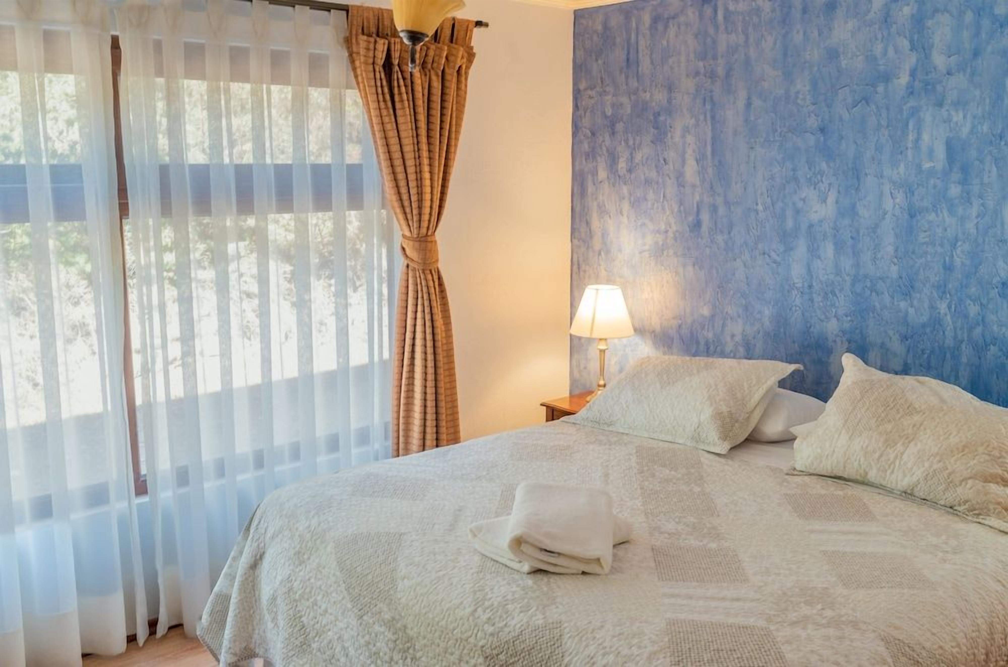 A bedroom with a bed, curtains, a lamp, and a blue wall.