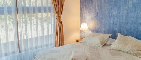 A bedroom with a bed, curtains, a lamp, and a blue wall.