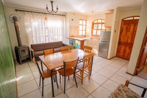 Un comedor con una mesa y sillas de madera, un sofá, una cocina con refrigerador y una puerta de madera.