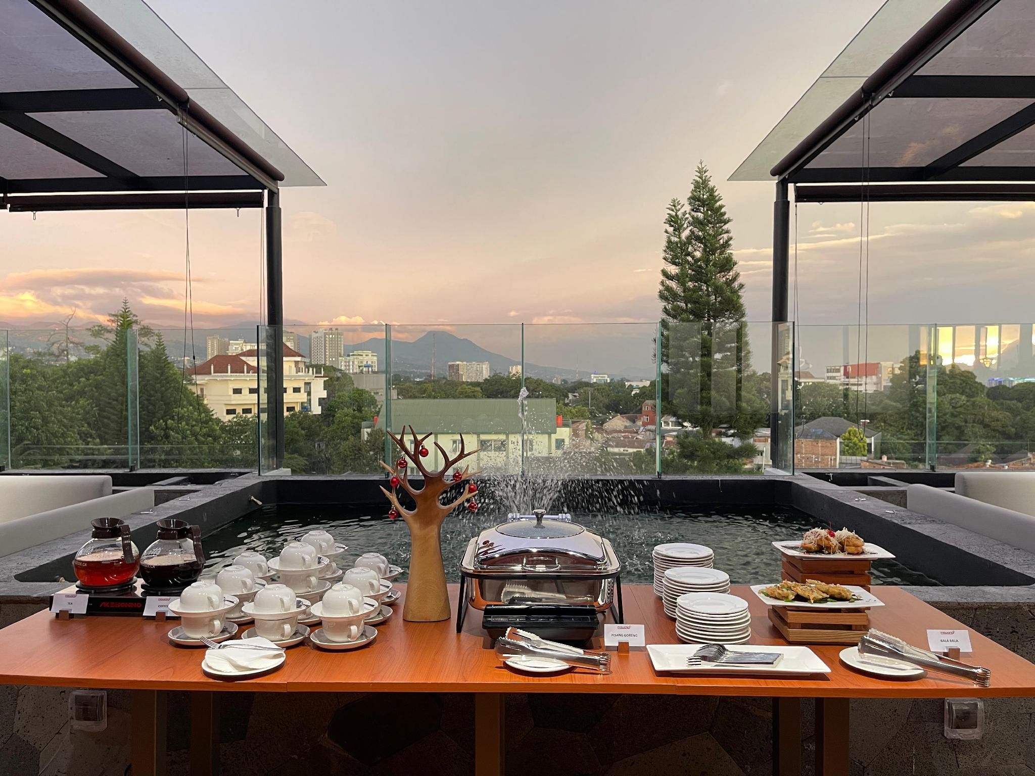 A rooftop dining area with a view of a cityscape, a decorative tree, and a table set with plates, cups, and a teapot.
