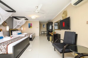 Una habitación de hotel con cama, mesita de noche, silla, televisión y ventilador de techo.