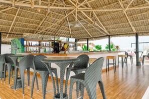 An indoor seating area with wicker chairs and tables, a bar with bottles, and a thatched roof structure. - Canary Kendwa (Kendwa)