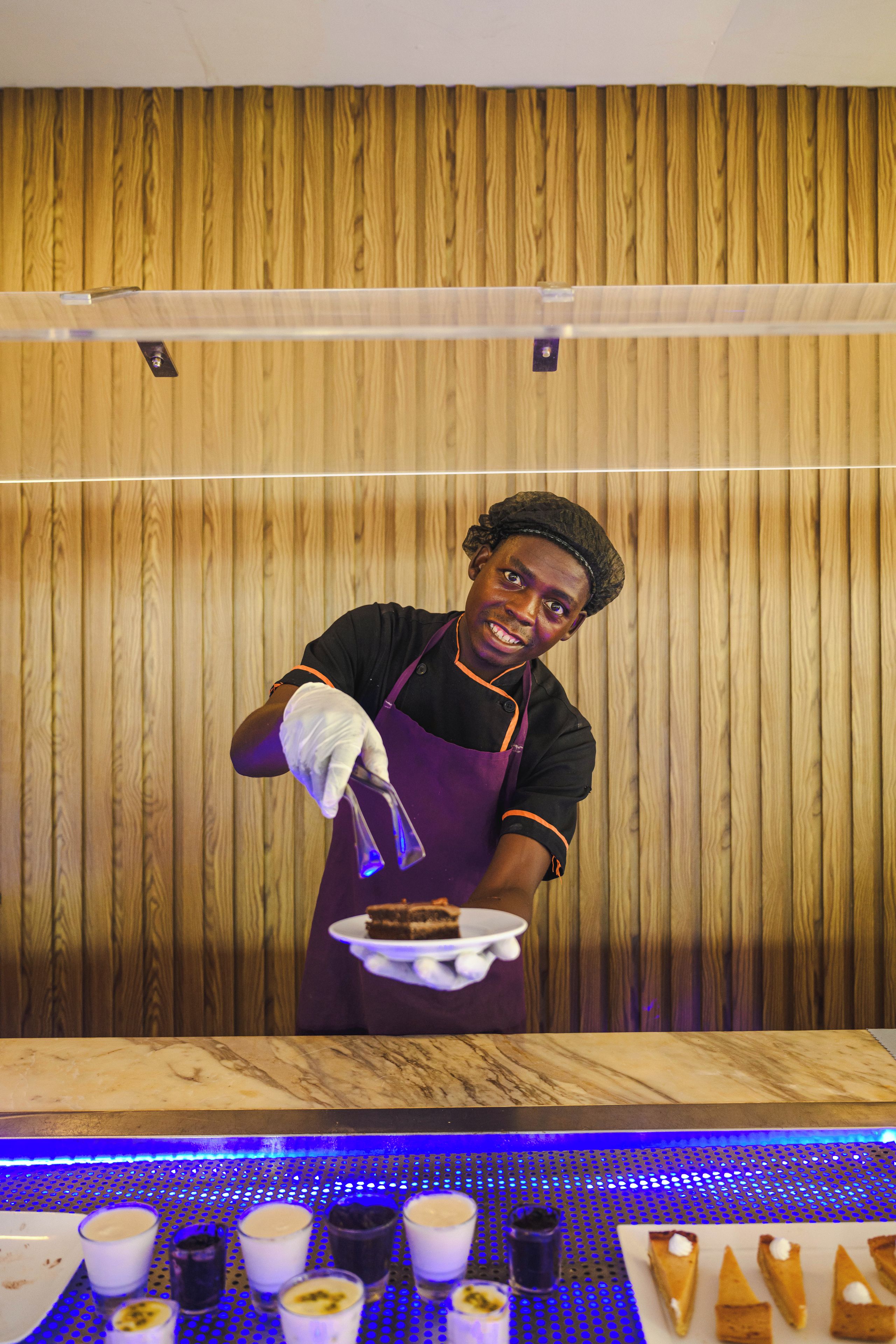 Une personne en uniforme, qui travaille derrière un comptoir en préparant et en servant des plats, avec un décor en bois en arrière-plan.