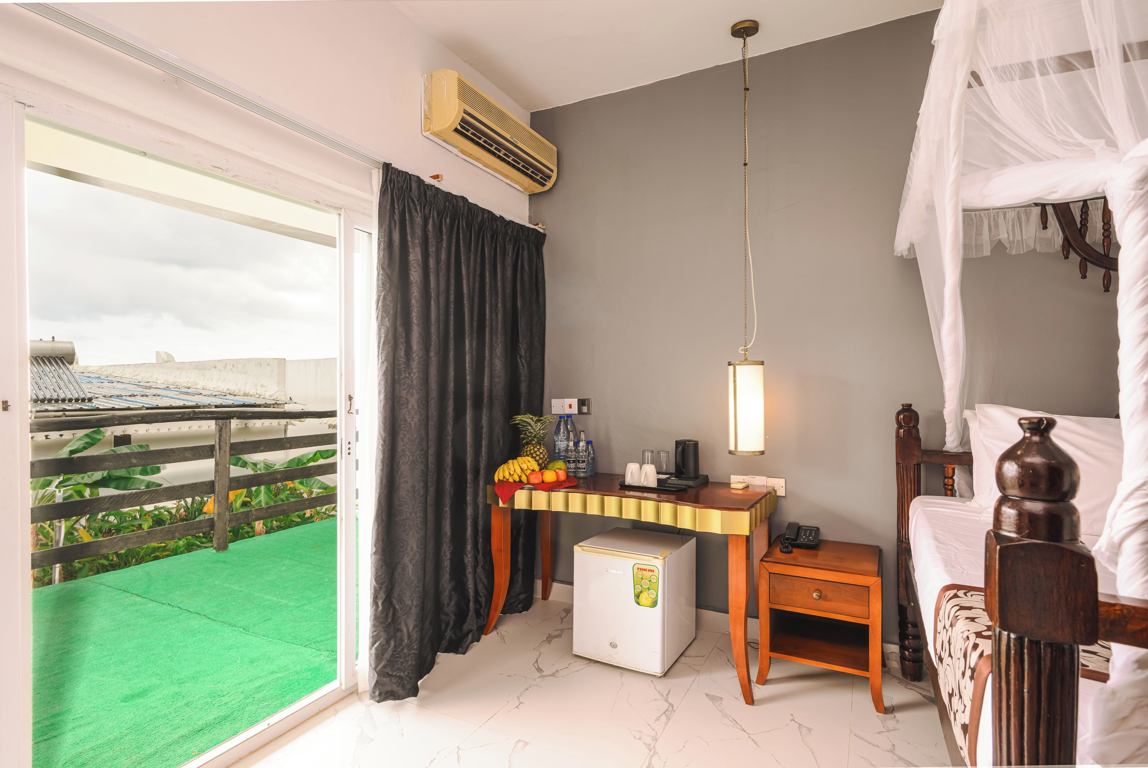 Une chambre d’hôtel comprenant un lit, un bureau avec un mini-bar, une fenêtre donnant sur un espace verdoyant et un appareil de climatisation.