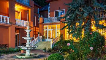 Un edificio de varios pisos con una escalera central, una fuente y un jardín con bancos y flores.