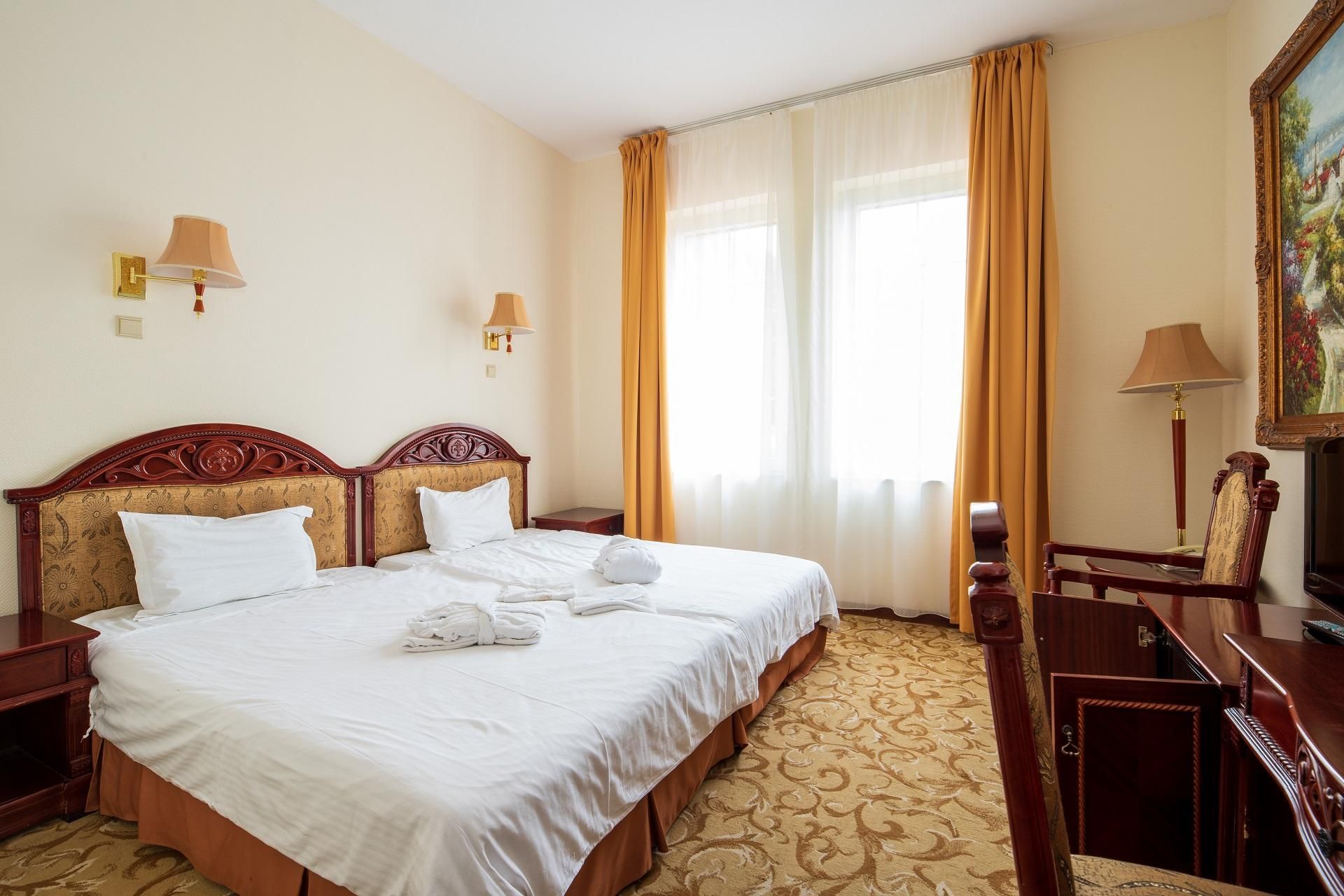 Habitación de hotel con una cama grande, dos mesitas de noche, un escritorio, una silla, un cuadro y cortinas.