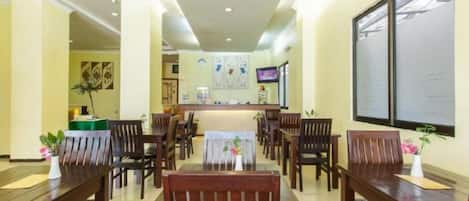 A hotel lobby with a reception desk, multiple wooden tables and chairs, and artwork on the walls.