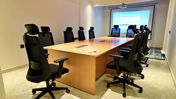 A conference room with a long table, black office chairs, and a projector screen displaying a presentation.