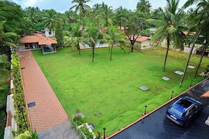 Zona residencial con un sendero pavimentado, un espacio de estar cubierto y un césped con palmeras.