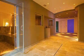 A modern interior with a glass-enclosed shower area, a stone-tiled floor, and a door leading to another room. - Le Blanc (Trento)