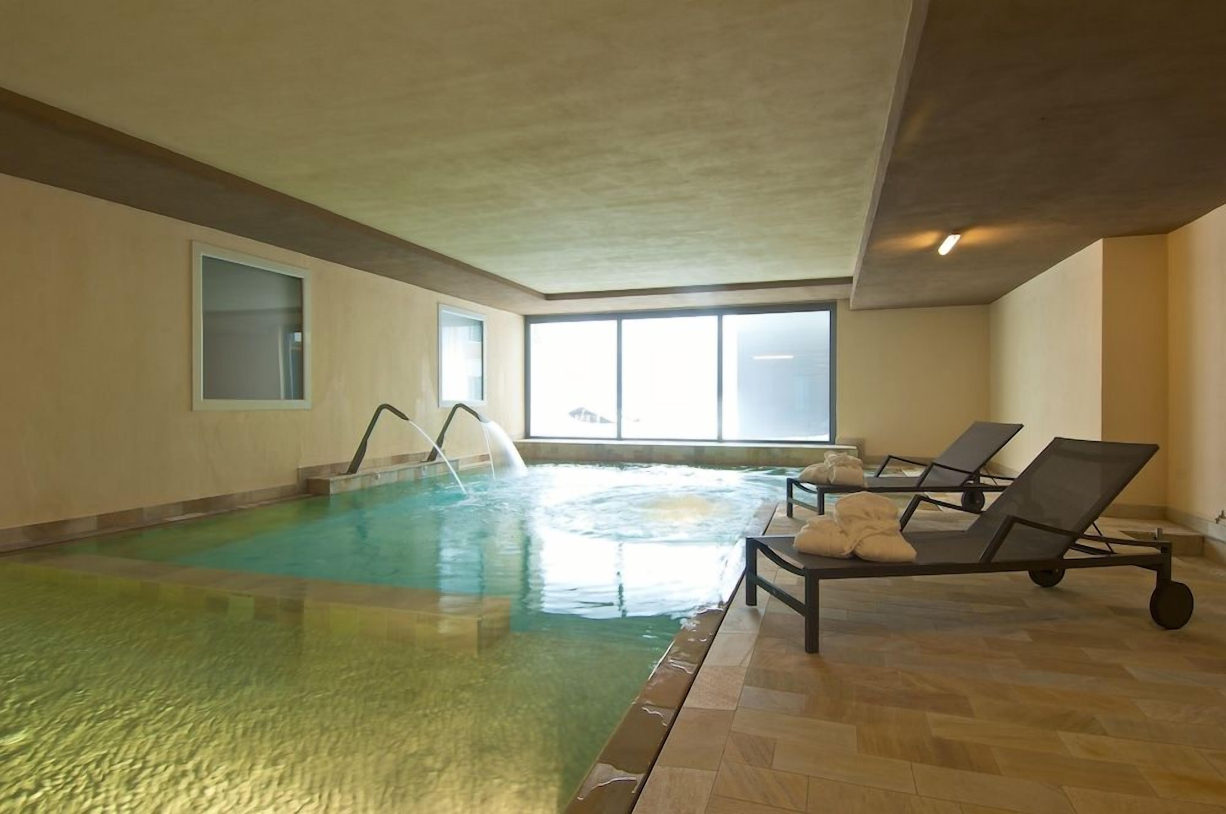 An indoor swimming pool with a clear view of the sky through large windows, a water slide, and lounge chairs with towels.