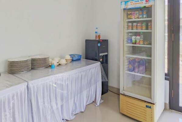 A room with a table covered by a white tablecloth, a refrigerator stocked with beverages, and a blue water dispenser. - Urbanview Hotel Praoe Lajar Tegal (Tegal)