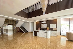 Un vestíbulo amplio con piso de mármol, una recepción y una escalera que sube a un nivel superior.