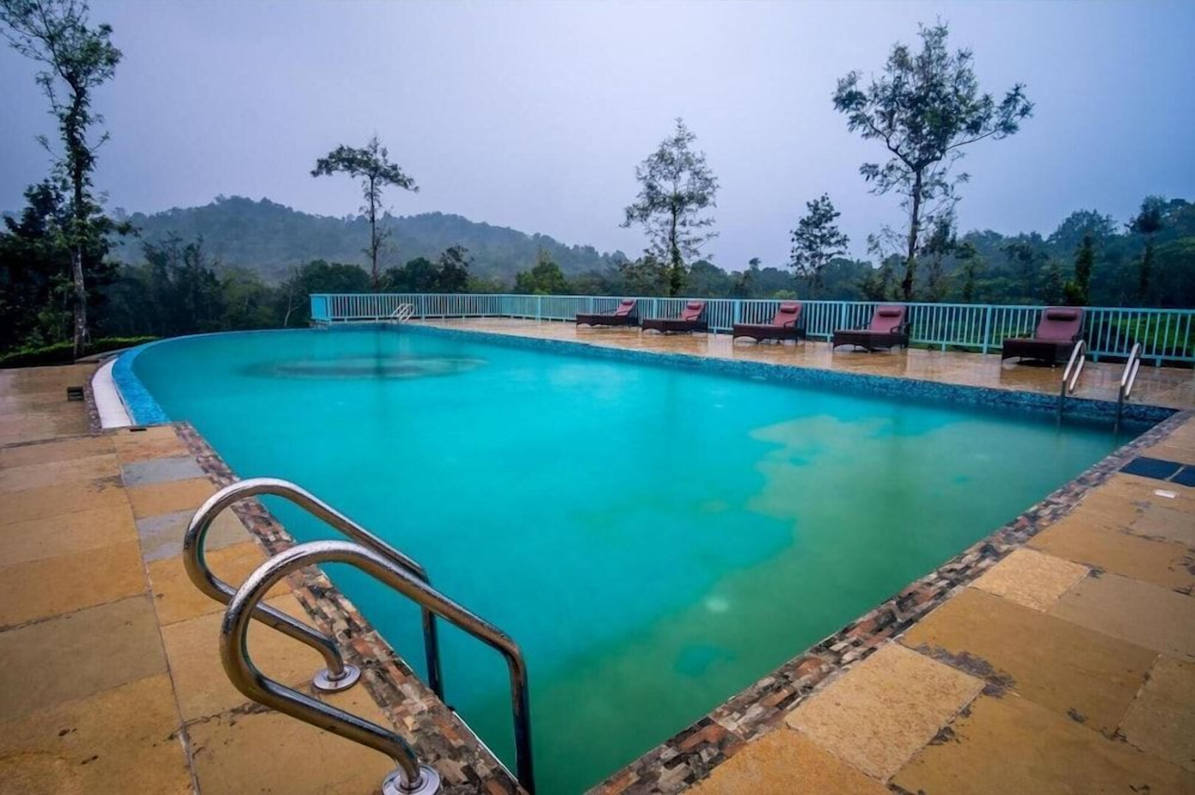Una piscina con borde de baldosas, rodeada de sillones de descanso y barandilla, con vistas a colinas al fondo.