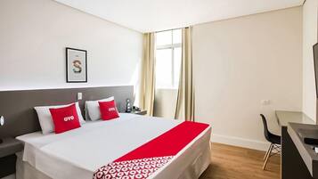 Quarto de hotel com uma cama, uma escrivaninha e uma cadeira.