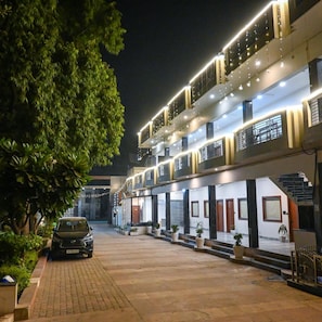 A multi-story building with a car parked in front, potted plants, and a well-lit entrance. - Hotel Kedar Dham (Mathura)