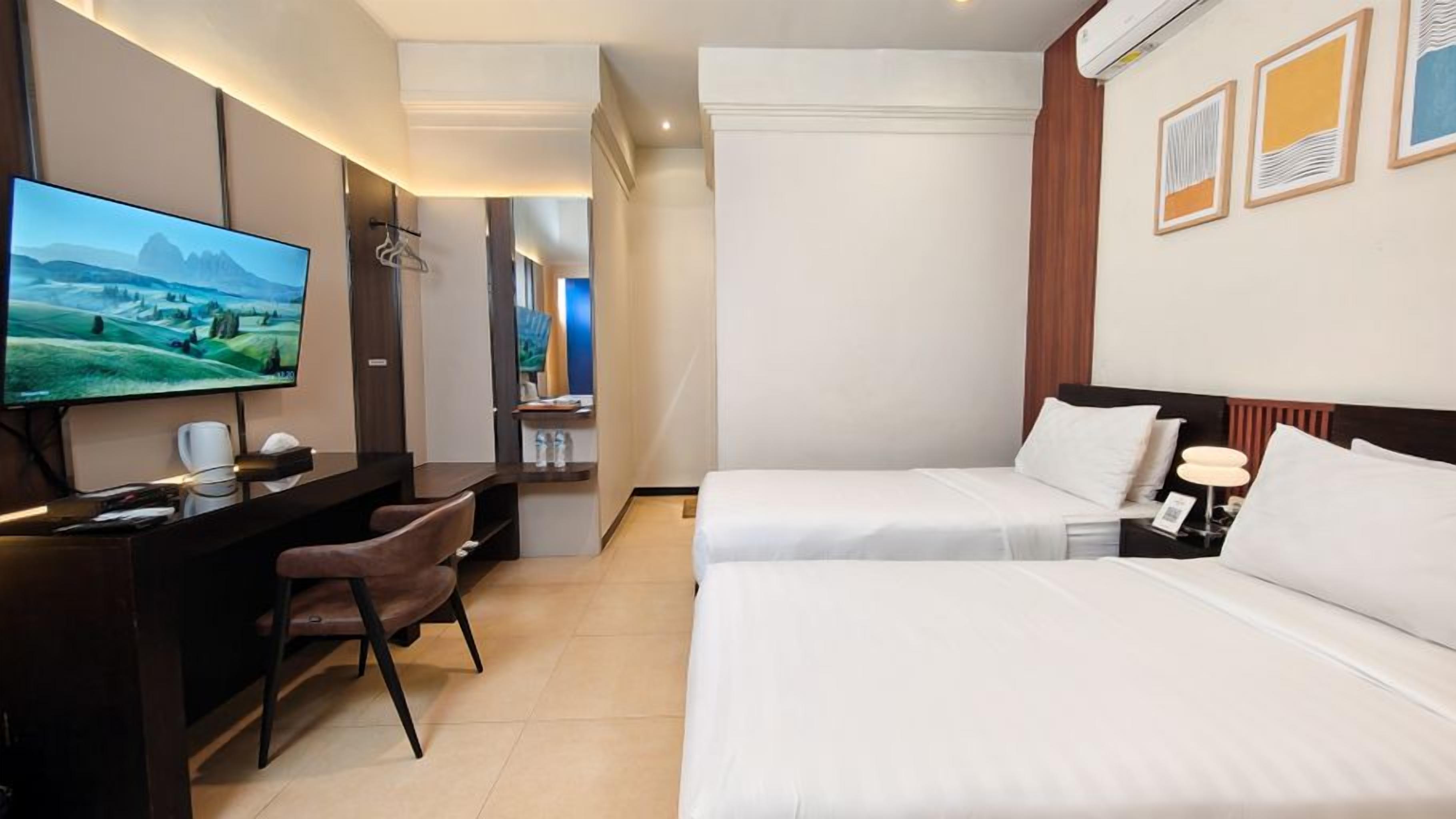 Ein Hotelzimmer mit einem Bett, einem Schreibtisch mit Stuhl, einem Fernseher und einem an der Wand befestigten Spiegel.