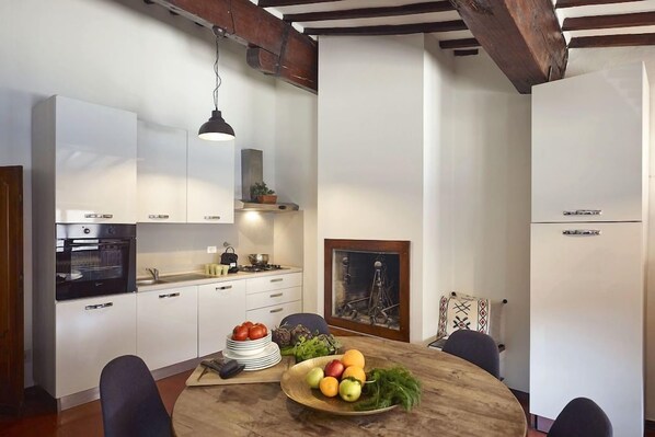 A modern kitchen with white cabinets, a wooden dining table, and a hanging pendant light.