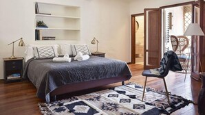 A bedroom with a bed, bedside tables, a chair, a bookshelf, and a door leading to another room.