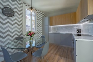 A modern kitchen with a glass dining table, grey and white chevron-patterned walls, and wooden cabinets.