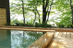 Una terraza de madera con piscina, rodeada de árboles y follaje.