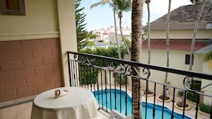 Un balcón con mesa y sillas, con vistas a una piscina y una zona residencial.