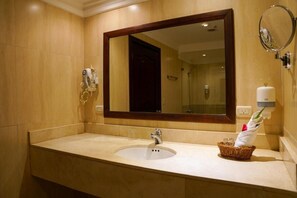 Une salle de bain d’hôtel avec un grand miroir, un lavabo et un distributeur de serviettes.