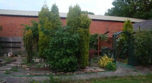 Ein Garten mit verschiedenen Pflanzen und einem Backsteinhaus im Hintergrund.