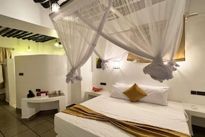Habitació d'hotel amb llit, taules de nit, mirall i finestra amb cortines.