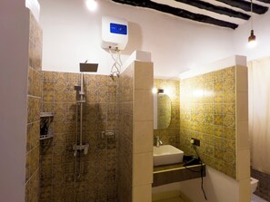 Et badeværelse med mønstrede fliser, en bruser, håndvask og toilet.