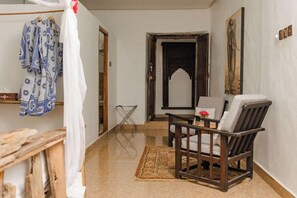 A room with a wooden chair, a small table with a vase, a patterned rug, and a doorway leading to another room. - Zanzi House (Zanzibar Town)