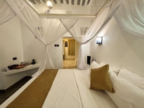 A room with a bed, a bedside table, a lamp, and a view of a bathroom. - Zanzi House (Zanzibar Town)