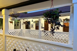 A covered outdoor area with white lattice railings, hanging plants, and a view of a building with multiple doors and windows. - Zanzi House (Zanzibar Town)