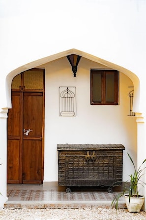 Una porta d'arc blanca de fusta, un fanal metàl·lic, un petit armari i una planta en test.