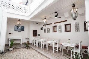 A dining area with white tables and chairs, decorative wall art, and ceiling fans. - Zanzi House (Zanzibar Town)