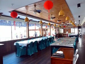 Um restaurante com mesas compridas, cadeiras e lanternas vermelhas penduradas.