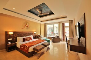 A hotel room with a large bed, a ceiling fan, a TV, and a view of the outdoors. - Summit By The Ganges Beach Resort & Spa (Rishikesh)