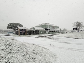 A building with a large porch and a covered area, surrounded by snow-covered ground and trees. - Ashburnham Hotel (Burry Port)