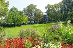 A well-maintained garden with a variety of flowers and trees, a grassy lawn, and a modern building in the background. - Favorite Parkhotel (Mainz)