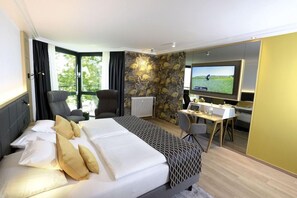A hotel room with a bed, a desk, a television, and a view of greenery outside. - Favorite Parkhotel (Mainz)