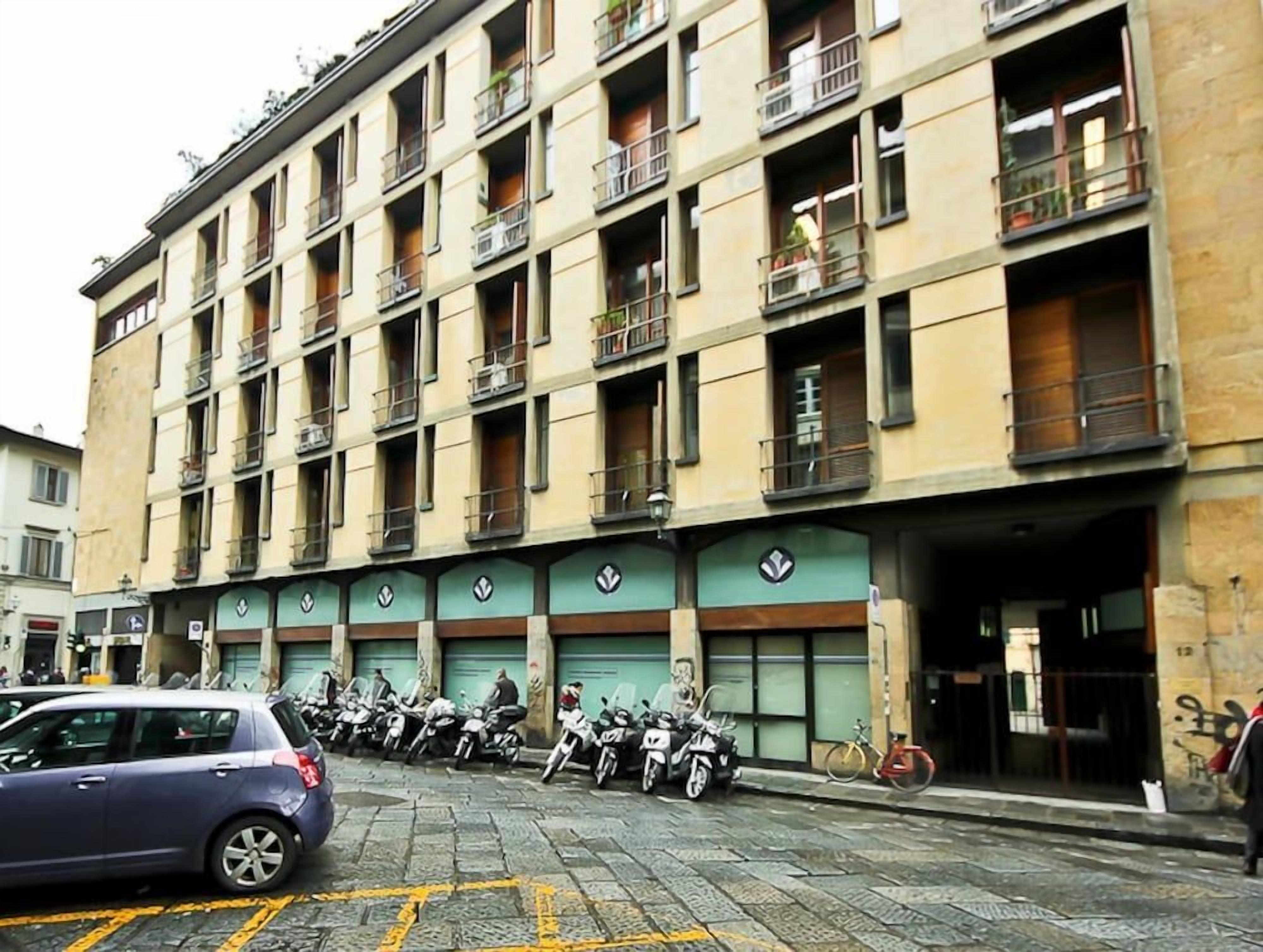 Un edificio a più piani con balconi, una fila di motociclette parcheggiate e un'auto in primo piano.