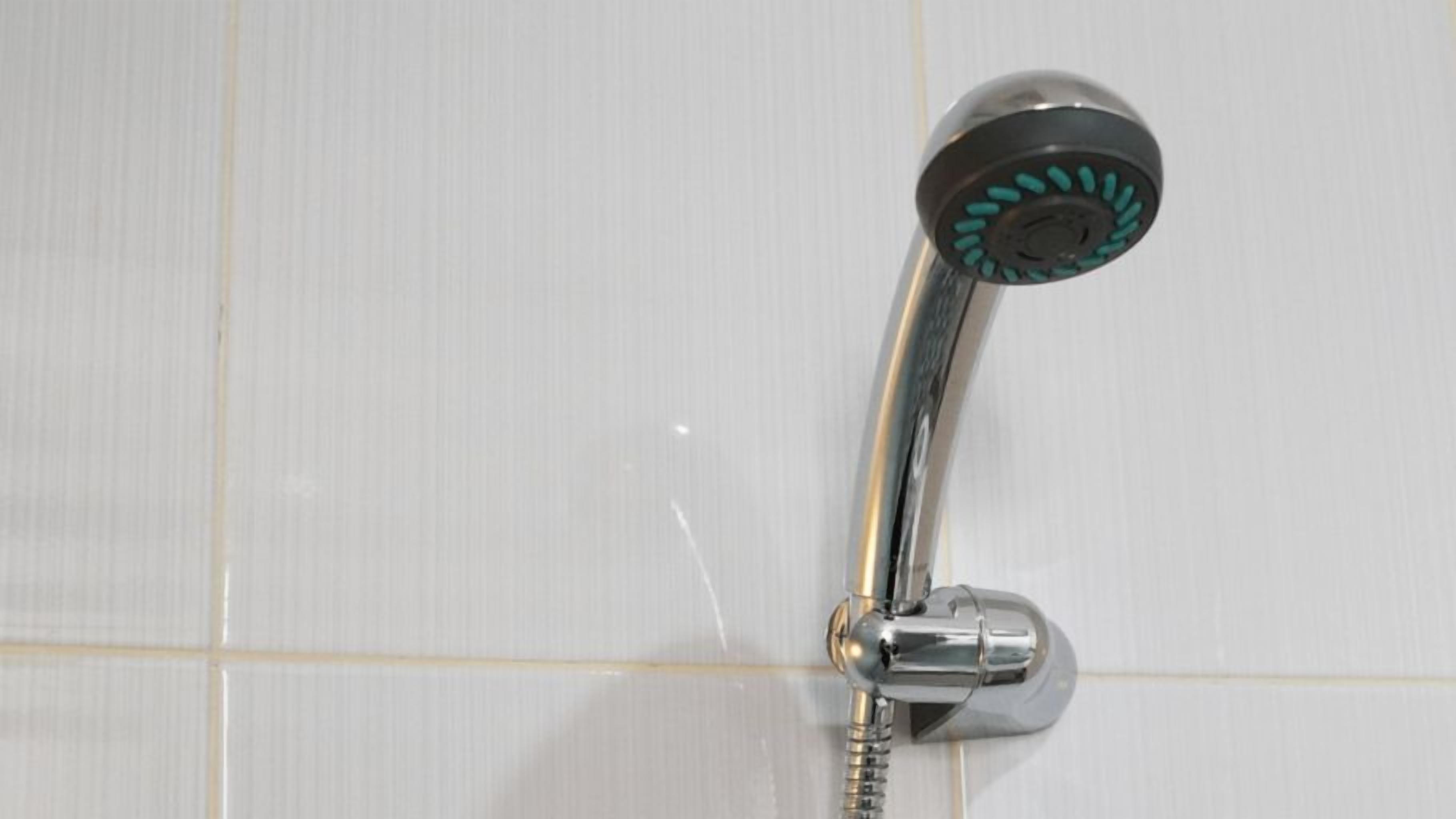 A chrome showerhead with a curved handle, mounted on a white tiled wall.