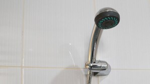 Un cabezal de ducha cromado con un mango curvo, fijado a una pared con azulejos blancos.