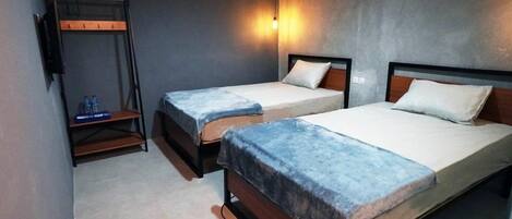 Une chambre d’hôtel avec deux lits simples, un banc avec des bouteilles d’eau et un téléviseur fixé au mur.