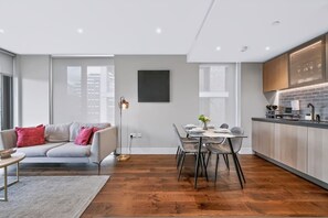 A modern kitchen with a dining area, wooden flooring, and a grey sofa with red cushions. - Modern 2 Bed Battersea Retreat Next to the Park (London)